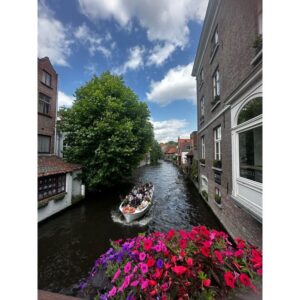 Tourists enjoy a scenic boat ride along a historic canal in Bruges, surrounded by flowers and architecture.